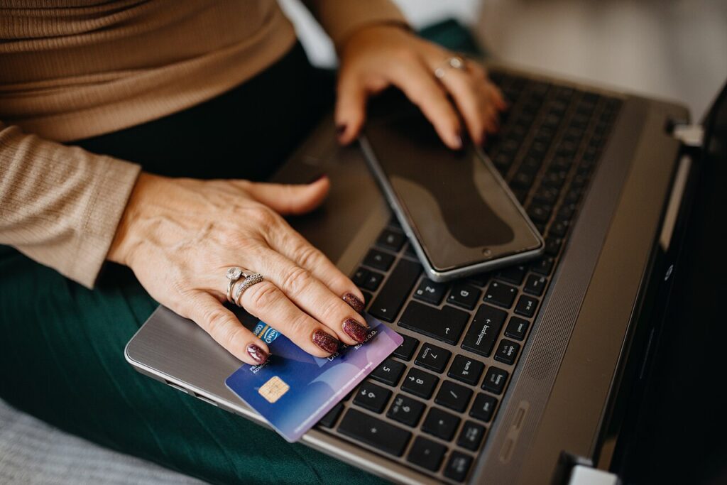 Mujer comprando en l&iacute;nea con tarjeta y celular sobre la laptop